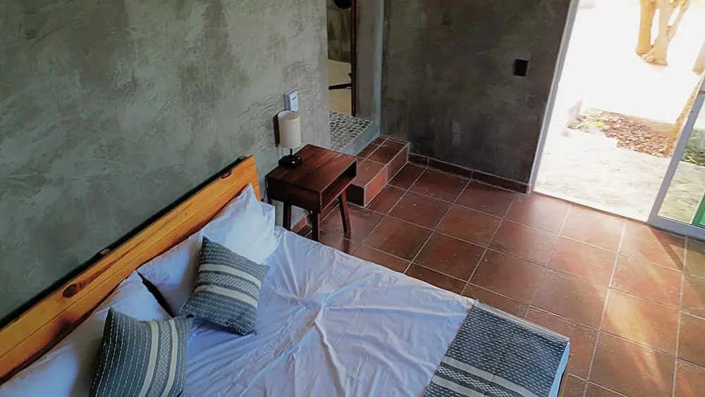 TIERRA Loft entrance with floor-to-ceiling windows, bed and gardens / Entrada a Loft TIERRA con ventanales de piso a techo, cama y jardines nativos